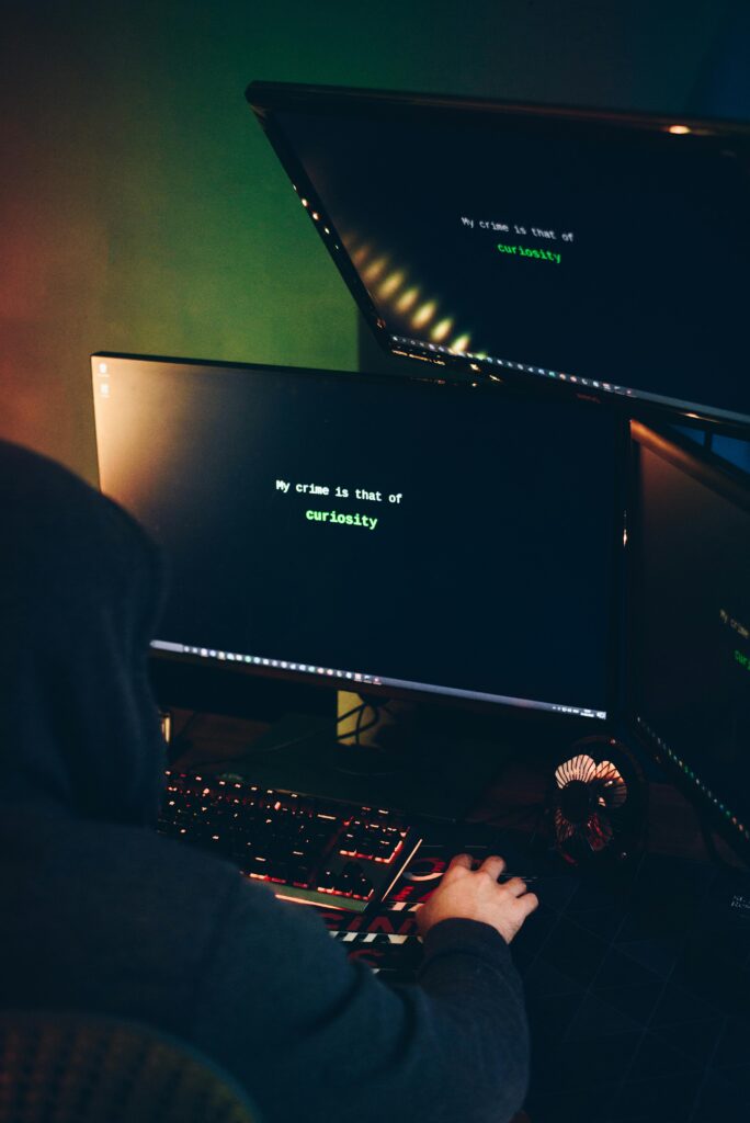 Membership A faceless individual using multiple monitors highlighting cybersecurity threats in a dark room.