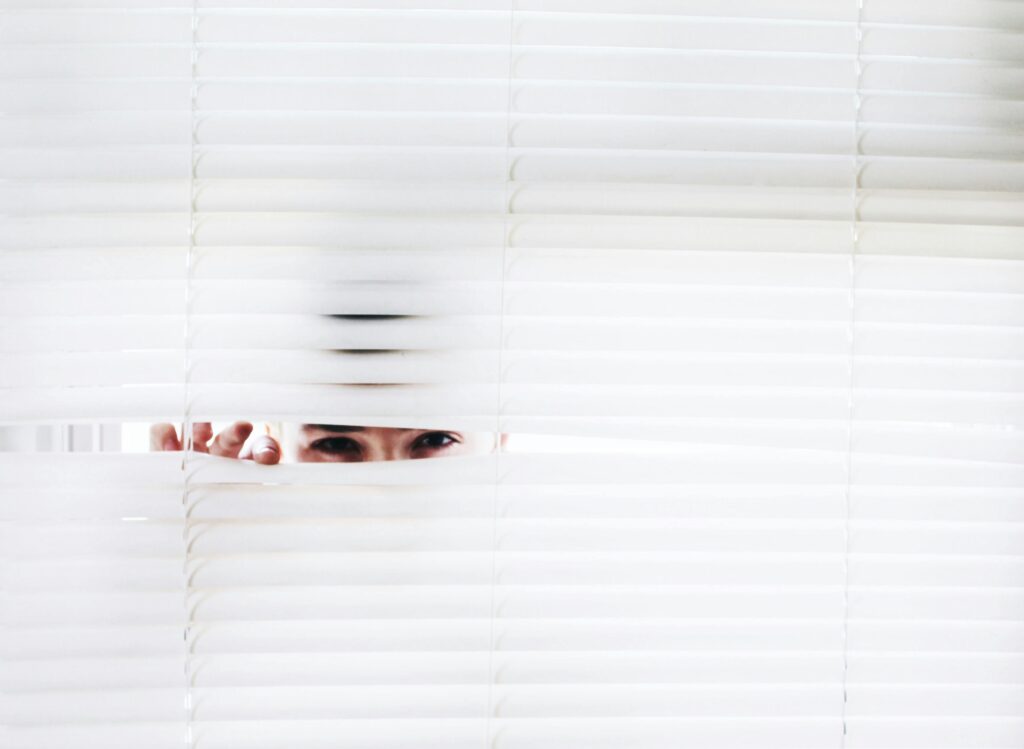 Membership A person peeks through white blinds, creating an intriguing sense of curiosity.